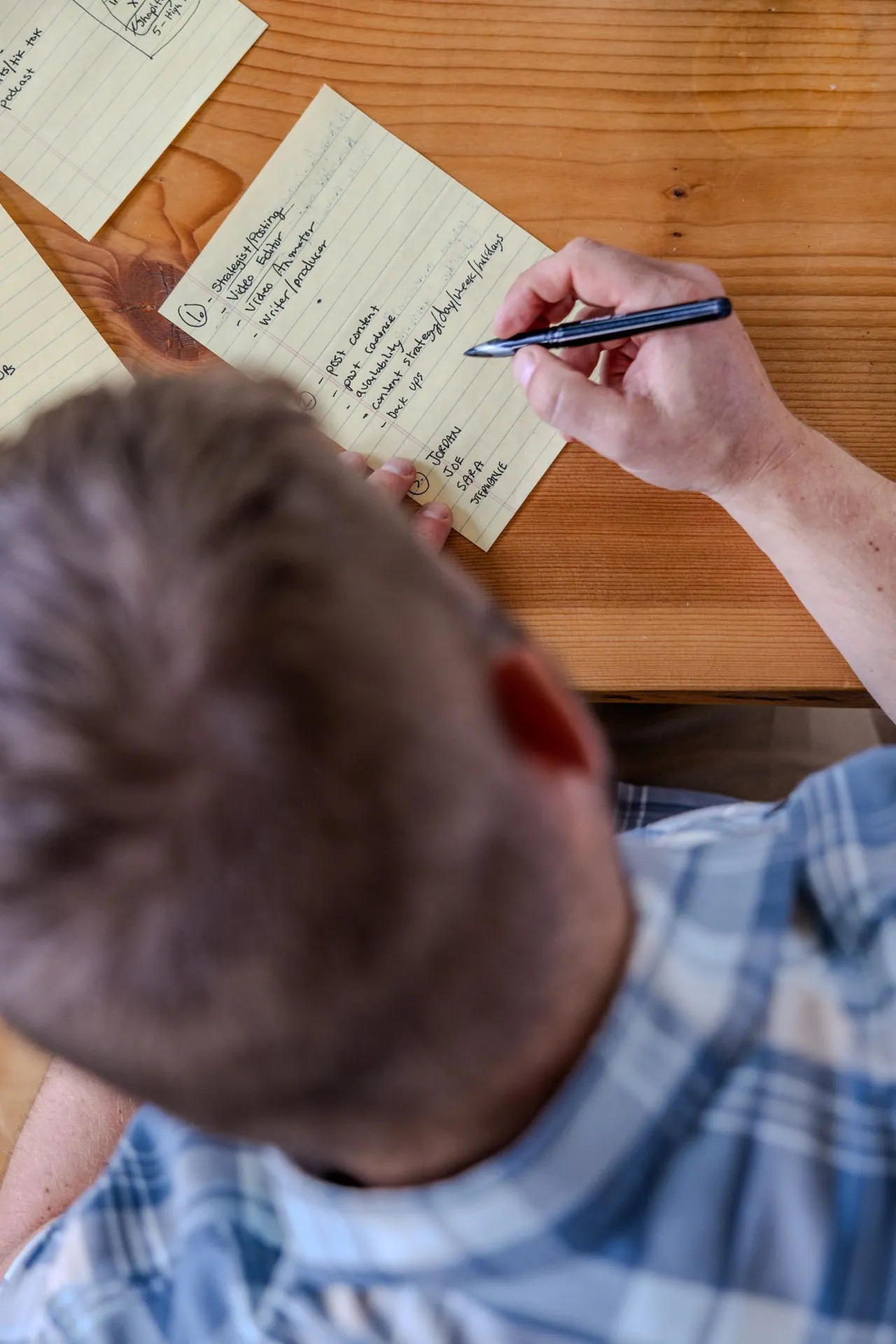 Overhead view of a person writing content production notes on a yellow notepad